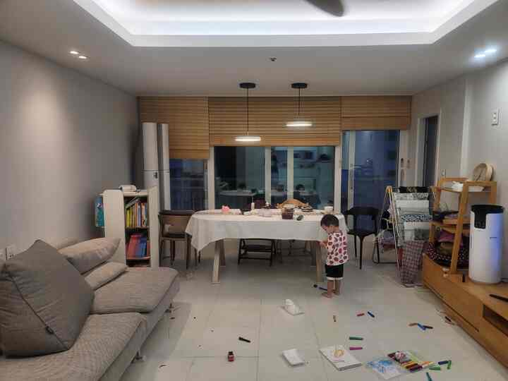 白い壁と木目調のブラインドが調和するリビング、ダイニングテーブルと床で遊ぶ赤ちゃんがいるリアルな育児空間