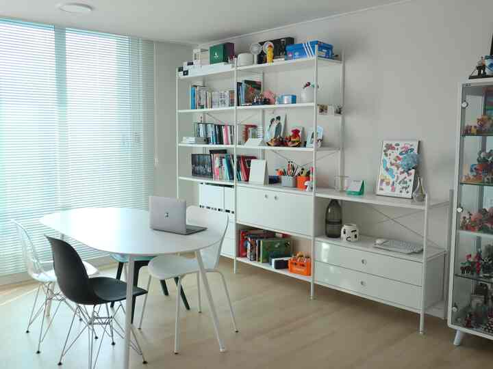 白と木目調が調和した書斎兼作業室、白い棚とテーブル、多様な椅子が配置されたすっきりしたインテリア