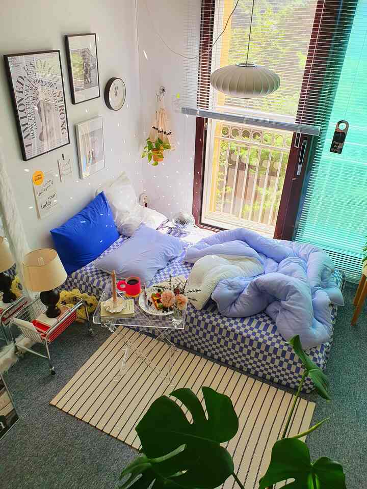A cozy bedroom featuring blue and white checkered bedding on the bed, pillows, and window blinds letting in natural light