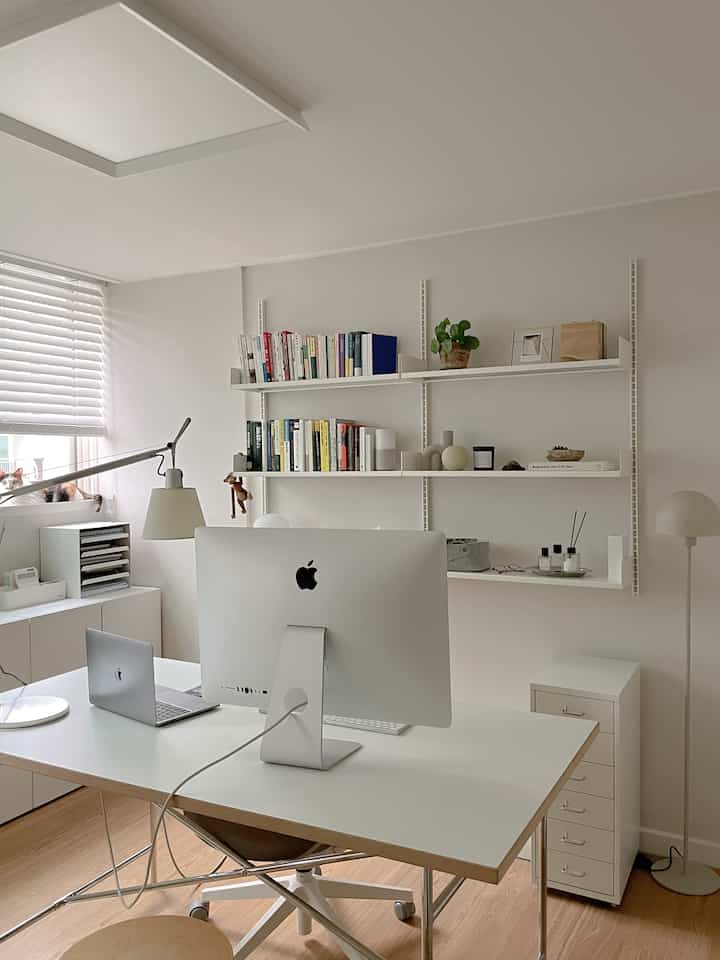 Bright white and natural tone study with desk and shelves neatly arranged with books and decor, creating a cozy atmosphere