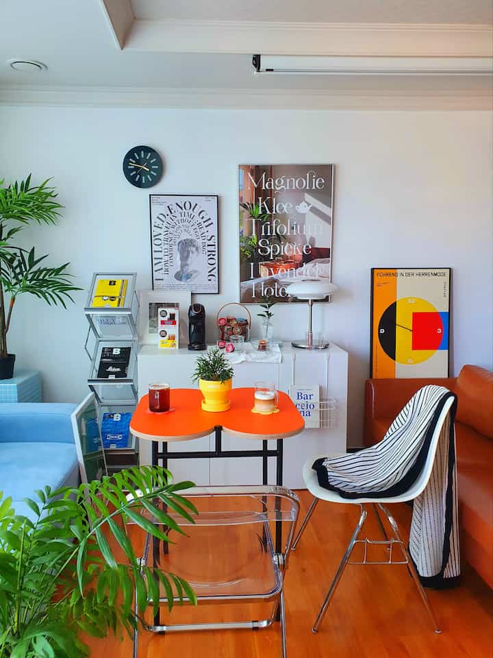 Bright white-walled living room featuring an orange dining table and mid-century modern furniture in a cozy home cafe setting