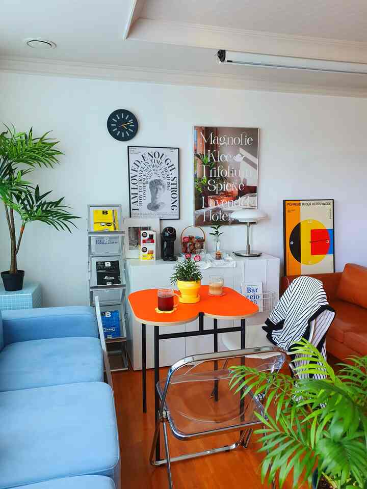 White-walled living room with orange and sky-blue sofas in mid-century modern style, featuring a cozy home cafe setup