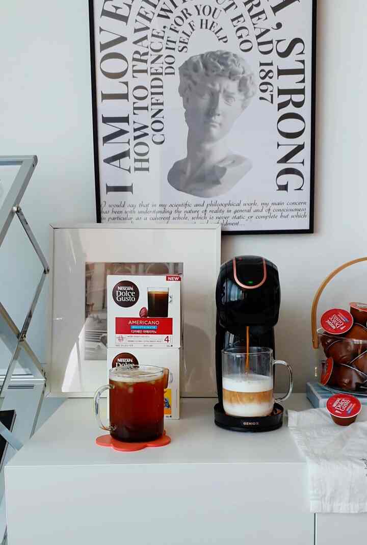 白と黒のトーンのキッチンスペース、コーヒーマシンとカプセルコーヒー、額縁が配置されたシンプルなホームカフェのインテリア