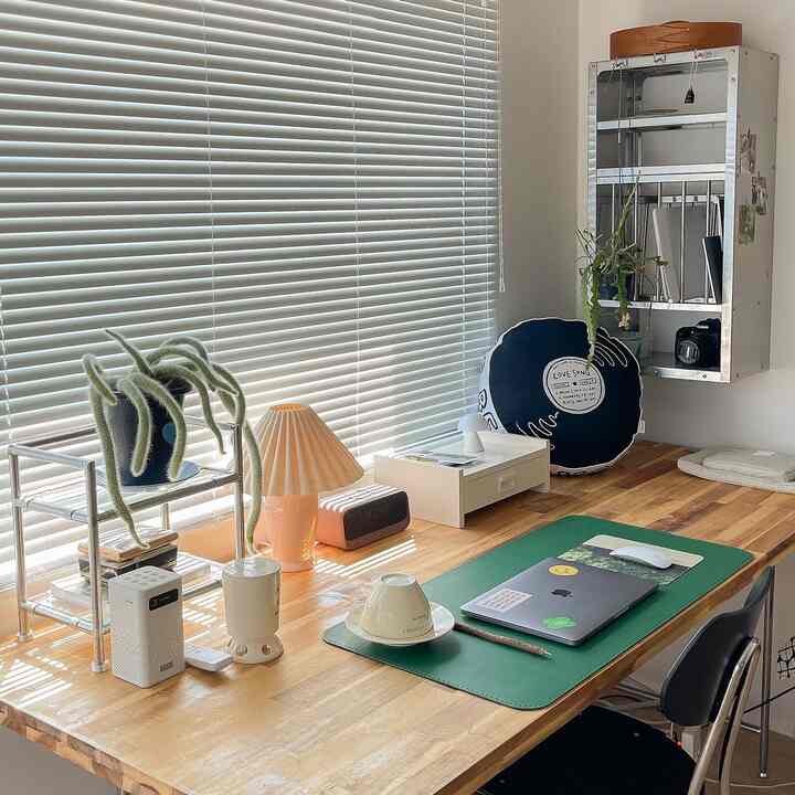 Wood tone and white study space featuring a green desk mat, vintage cushion, and plants in a warm home cafe style interior