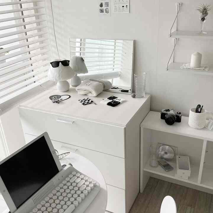 Bright modern white-toned living room featuring shelves and a desk neatly arranged with minimal accessories