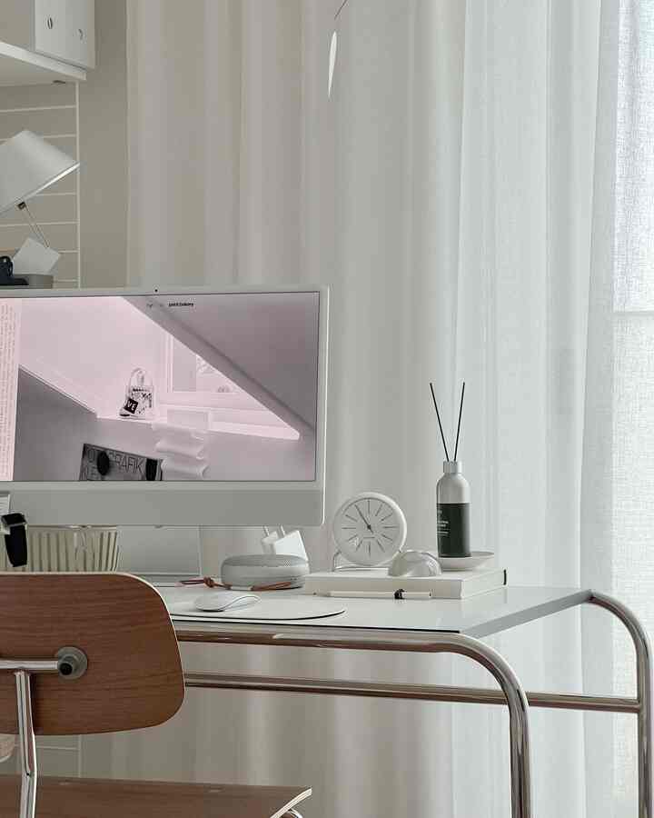White and beige toned home office featuring a clean desk, wooden chair, clock, and diffuser creating a simple modern interior