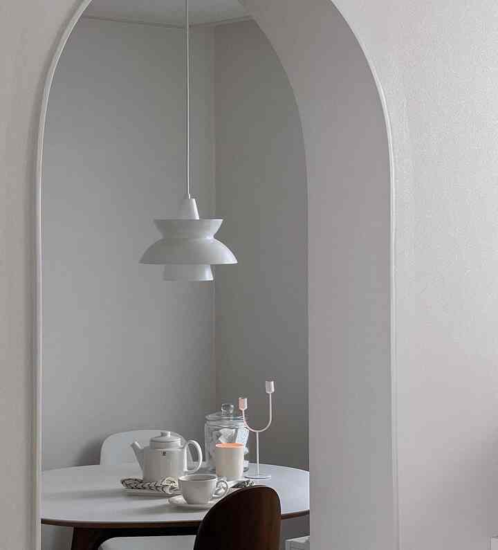 落ち着いたモノトーンのダイニングルーム、アーチ型の入り口の中に白いダイニングテーブルとペンダントライトが配置されたシンプルな空間