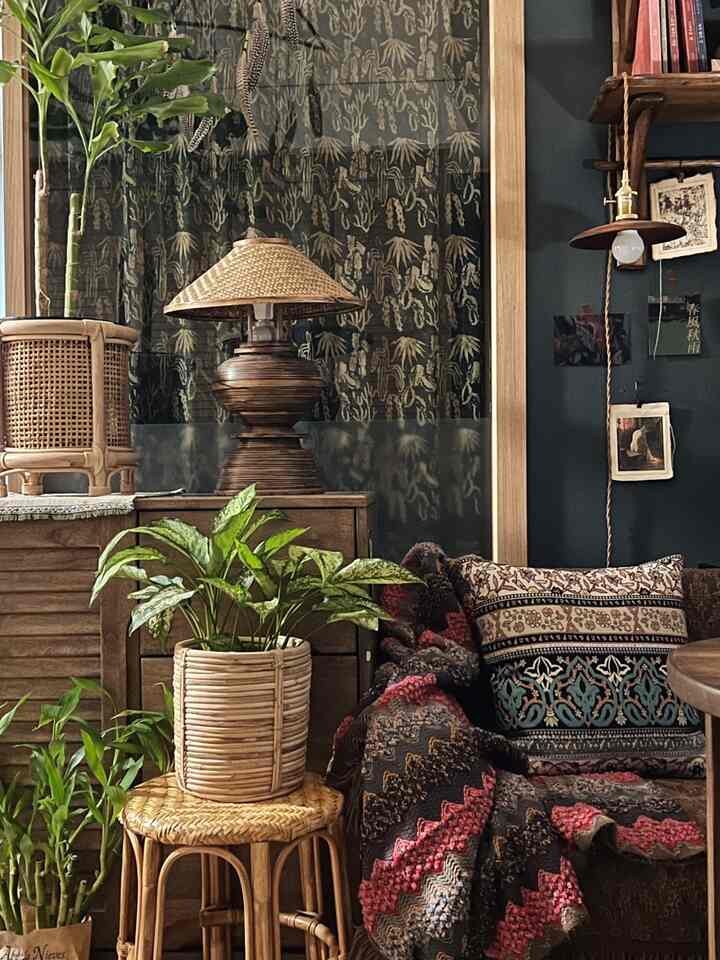 Cozy living room with dark green and brown wood tones, featuring ethnic patterned cushions and throw, rattan stool, and lush plants