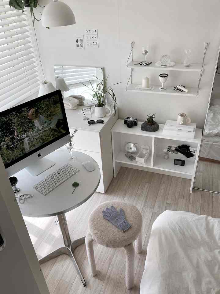 明るい白と木目調が調和するホームオフィス兼ダイニングルーム、丸いスツールとアイマック、棚が整然と配置された温かみのある空間