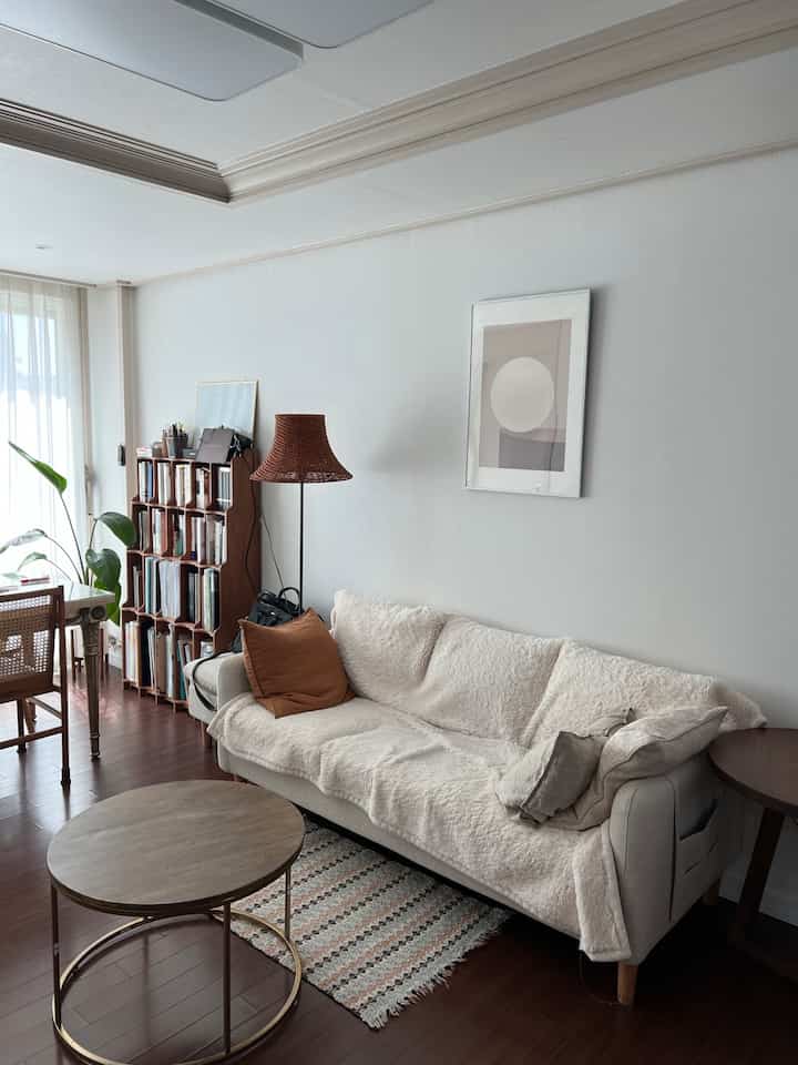 A clean living room with dark wood flooring and beige fabric sofa, featuring a round coffee table and rattan floor lamp in a natural atmosphere