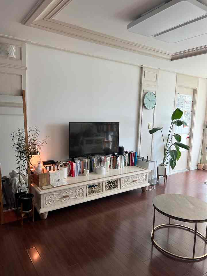 白い壁と象牙色の家具が置かれたリビングルーム、植物と丸いコーヒーテーブルが配置された雰囲気のあるフレンチカントリースタイルの空間