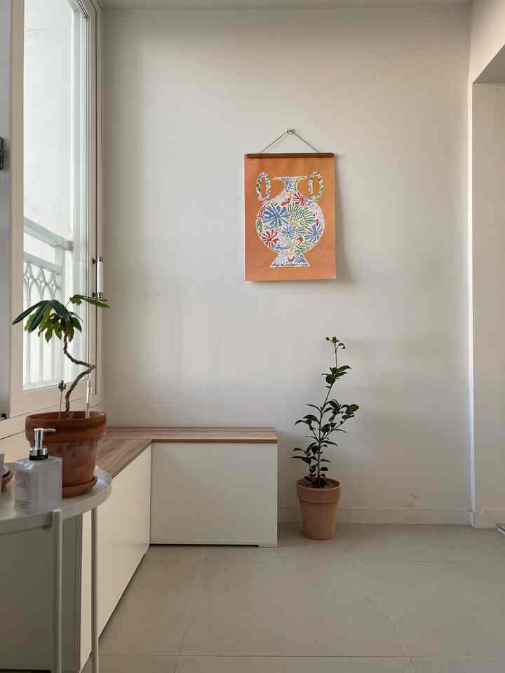 Minimalist entrance with white walls, wood-tone bench, plants, and a colorful urn painting