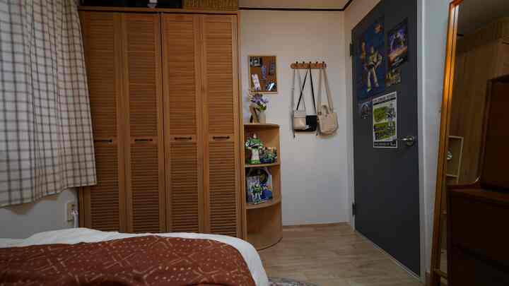Natural-toned bedroom featuring large wooden wardrobe and corner shelf displaying figures and accessories with cozy atmosphere