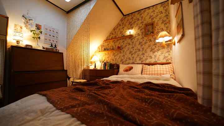 Cozy bedroom with wood tones and floral wallpaper, featuring wall sconces and shelves creating a warm atmosphere