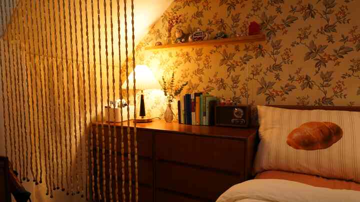 温かみのある木目調と黄色い光が漂う寝室、木製の収納とパン柄の枕が居心地の良さを演出するインテリア