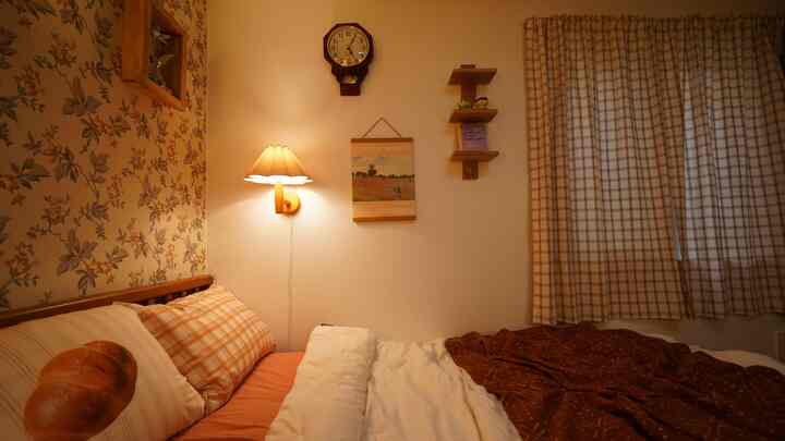 ベージュとブラウンのトーンの寝室、壁の棚、壁掛け照明、チェック柄カーテンが調和した雰囲気のあるインテリア