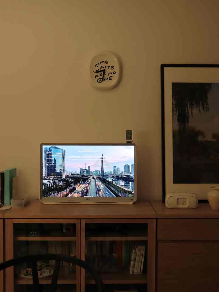 White-walled home office featuring a brown wooden TV stand, monitor, and framed art creating a sophisticated atmosphere