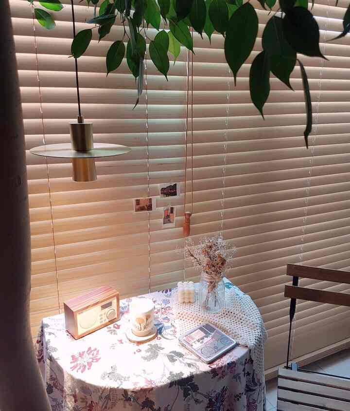 ベージュの木目調ブラインドと小さな花柄テーブルが配置されたカフェ風の小さな空間