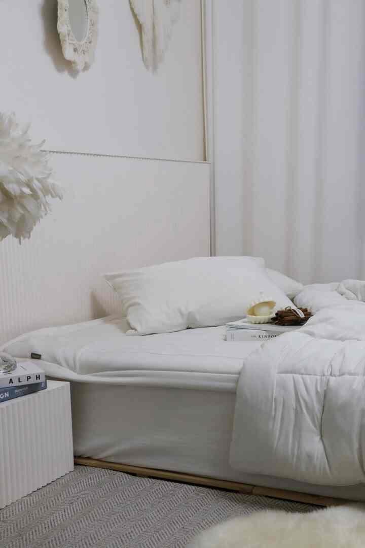 白とナチュラルトーンの寝室、整った白いベッドと枕、ラグが配置されたミニマルな雰囲気のインテリア