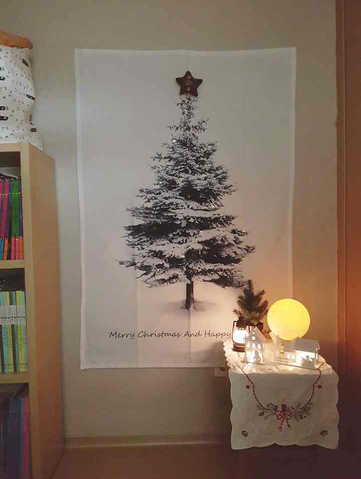 白とベージュの色調の子供部屋、中央に雪の積もったクリスマスファブリックツリーの壁飾りと暖かい照明が配置された雰囲気のあるインテリア