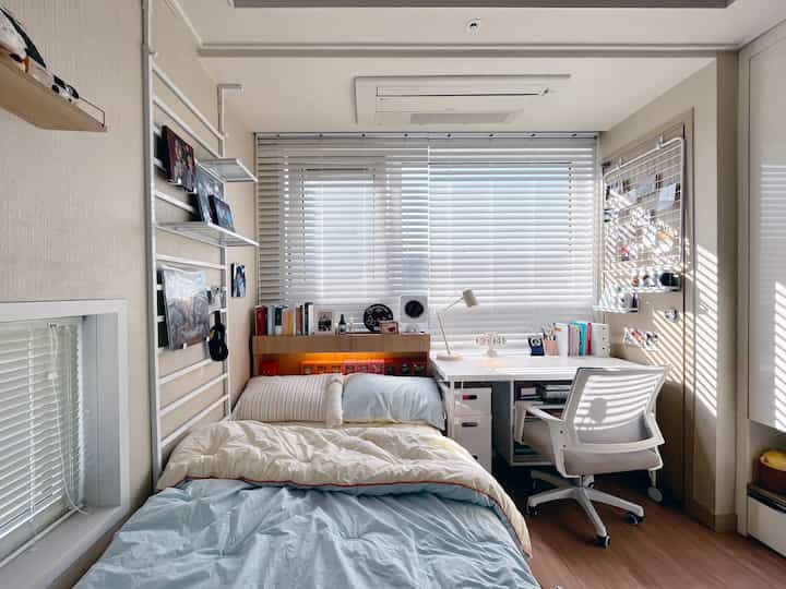 White and natural tone studio apartment featuring a bed, desk, and blinds with a clean and efficient interior