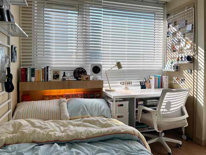 A bedroom with white blinds and natural wood tones featuring a desk and chair, creating a cozy home office and reading area