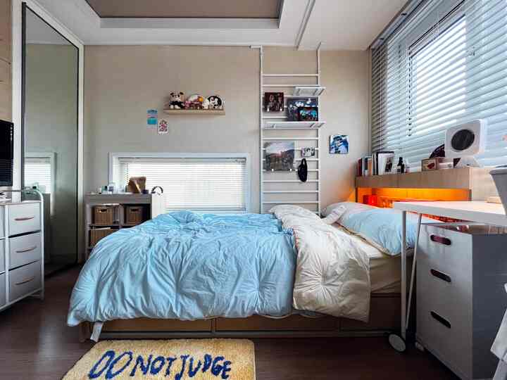 Sky blue bedding and beige walls harmonize in a bedroom featuring a bed, white dresser, and blinds creating a cozy atmosphere