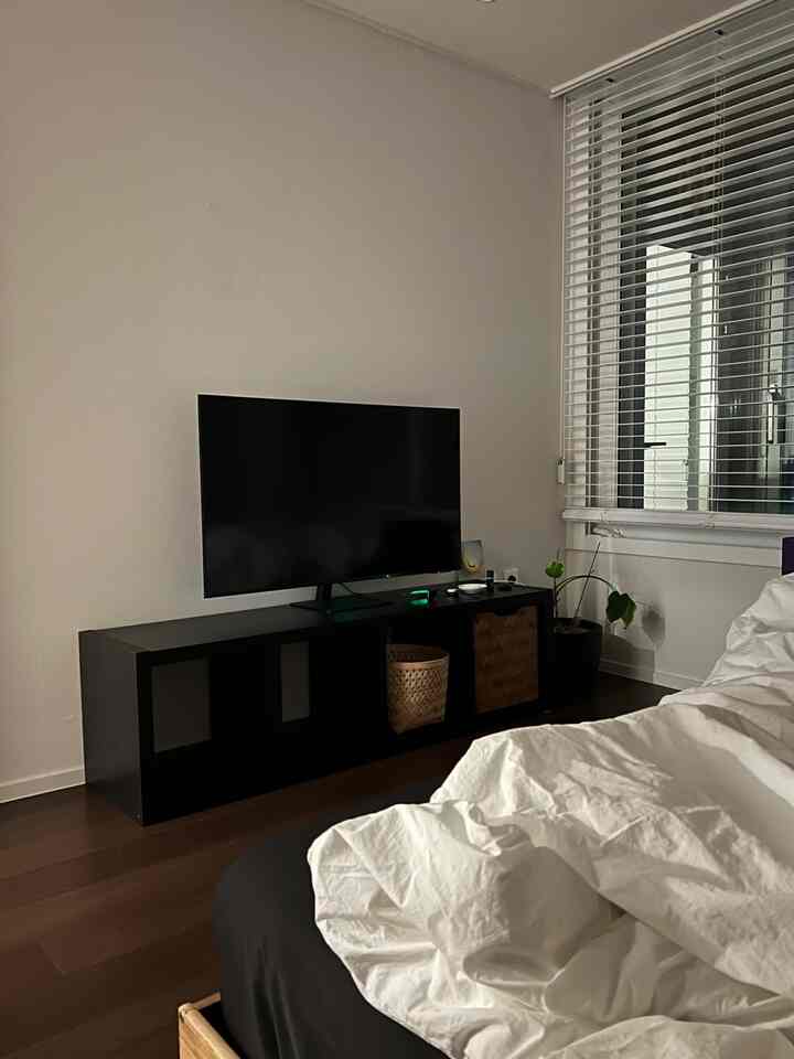 白い壁とブラインド、黒いテレビ台とベッドが配置されたシンプルな寝室のインテリア