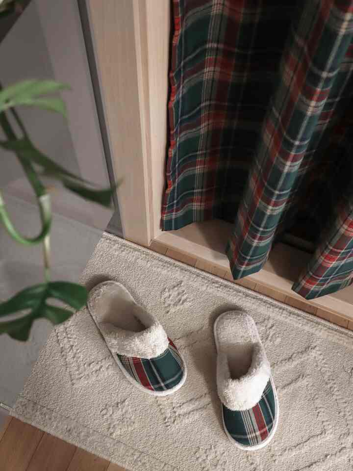 Cozy entrance area featuring green and red plaid curtains with fur-lined plaid winter slippers resting on a beige rug
