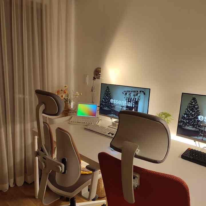 White and beige toned two-person home office featuring dual monitors and ergonomic chairs in a clean workspace
