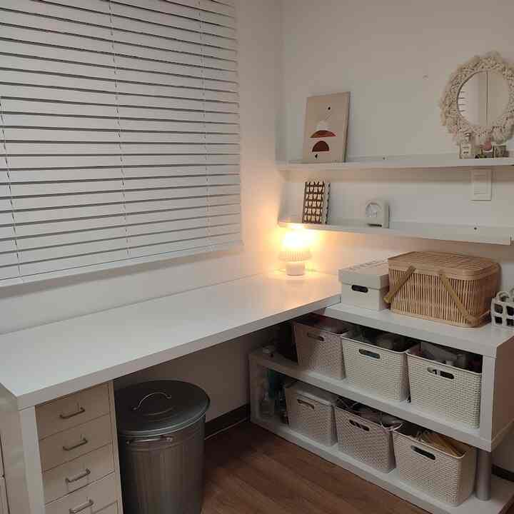 White and wood tone workspace featuring a large desk, shelves with storage baskets, and a table lamp with a simple interior design