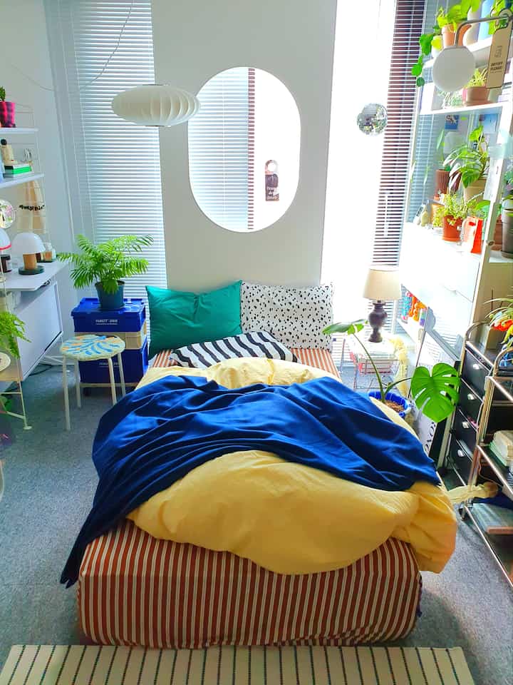 White and gray tone studio bedroom featuring colorful bedding and lush plants with cozy atmosphere