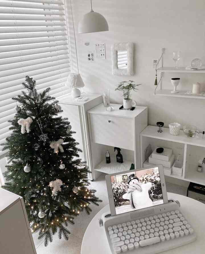 ホワイトトーンのコンパクトな部屋にグリーンのクリスマスツリーと白い家具、デスクが配されたシンプルでミニマルな雰囲気のインテリア