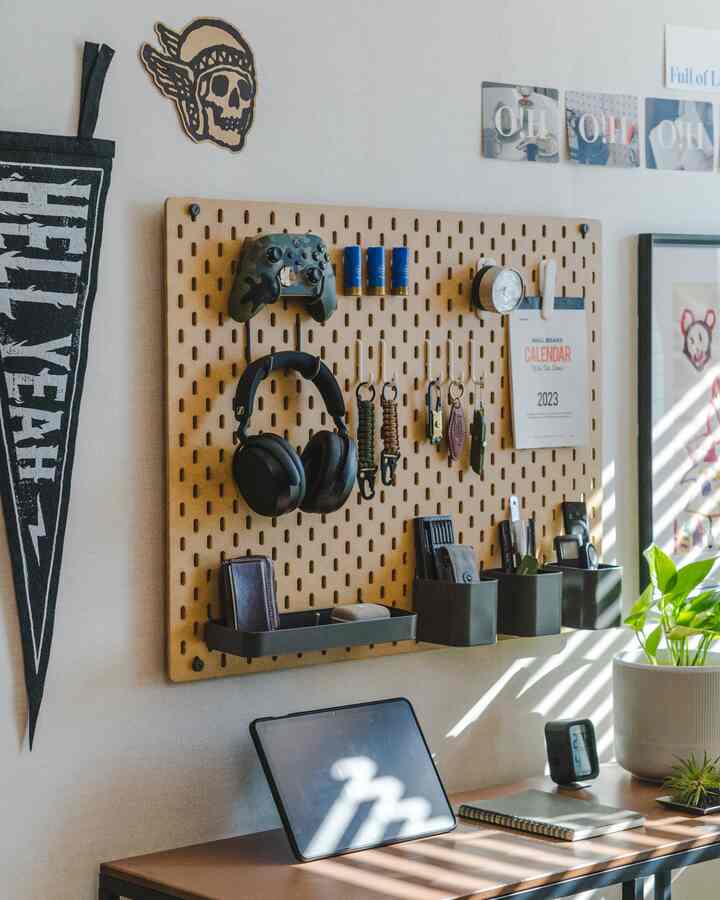 White-walled home office featuring a brown desk with a pegboard organizing gaming accessories and a tablet, accented by a green plant