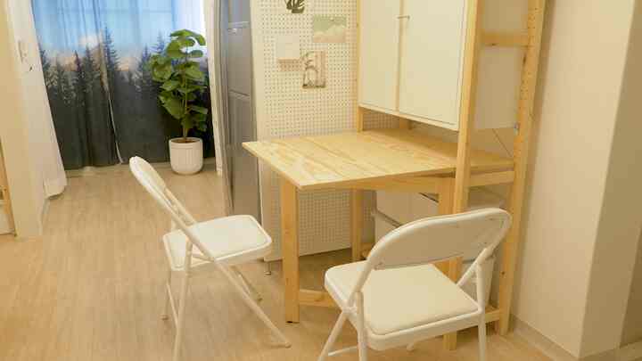 Compact space with bright wood tones and white elements, featuring folding chairs and a foldable desk arranged practically