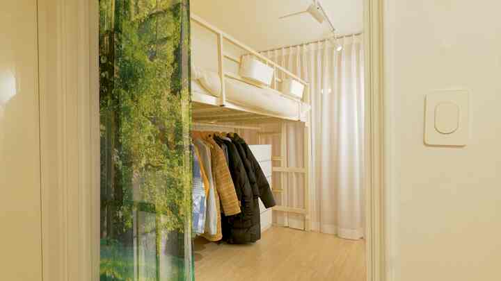 Bright white and wood tone long narrow room featuring a bunk bed, curtains, and clothes hangers creating a cozy atmosphere
