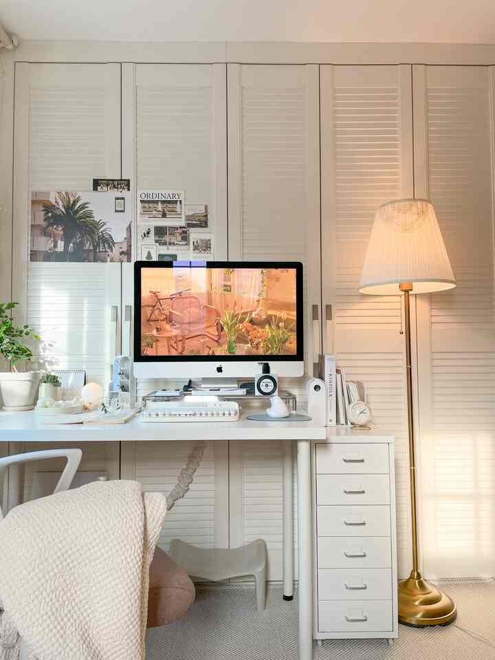 White-toned home office space featuring a white desk, dresser, plants, and monitor with a neat, modern interior