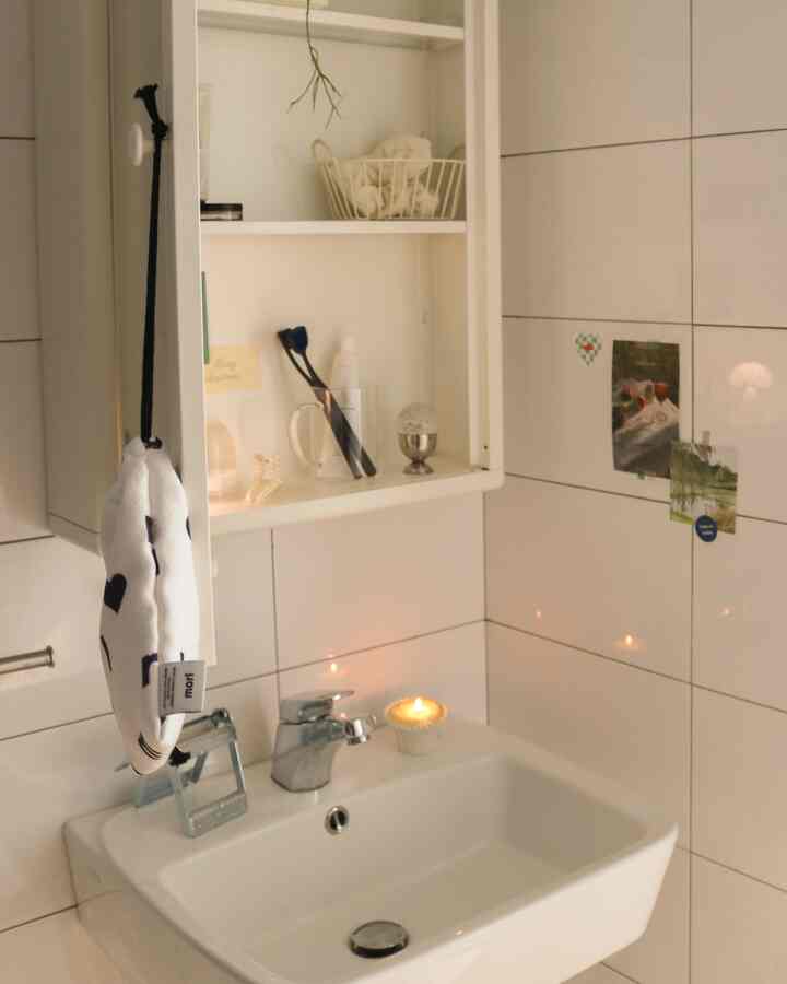 温かみのあるベージュと白の小さなバスルーム、洗面台と棚にかわいらしい小物が並ぶ清潔感のある空間