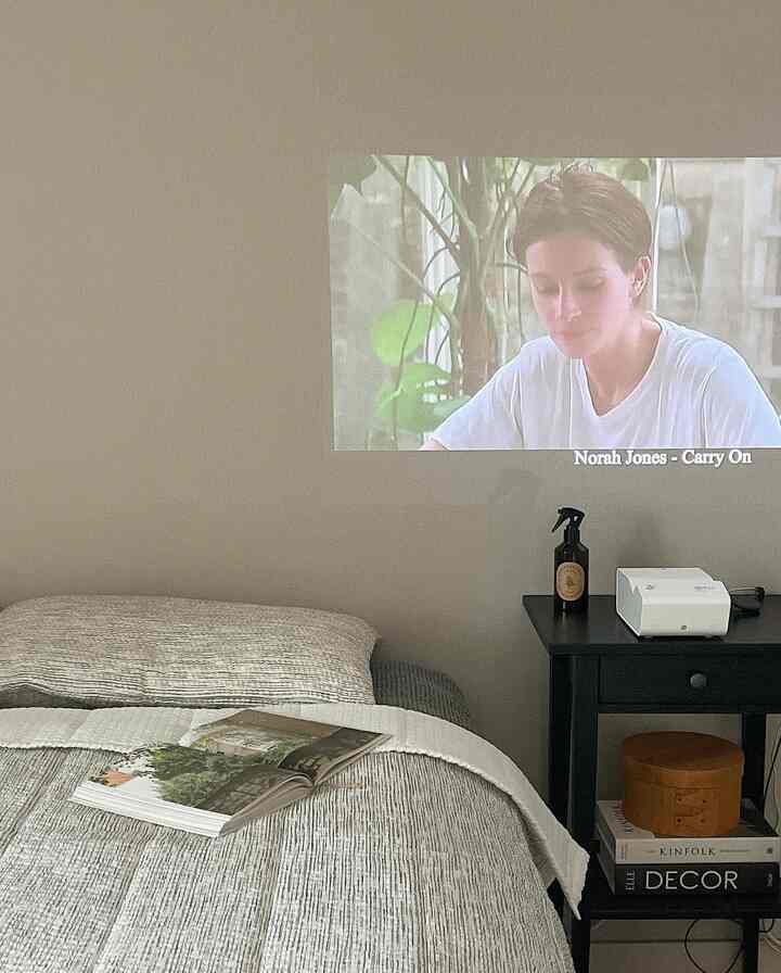 Gray and beige tone bedroom featuring a bed and small nightstand with a projector, creating a cozy home cinema environment