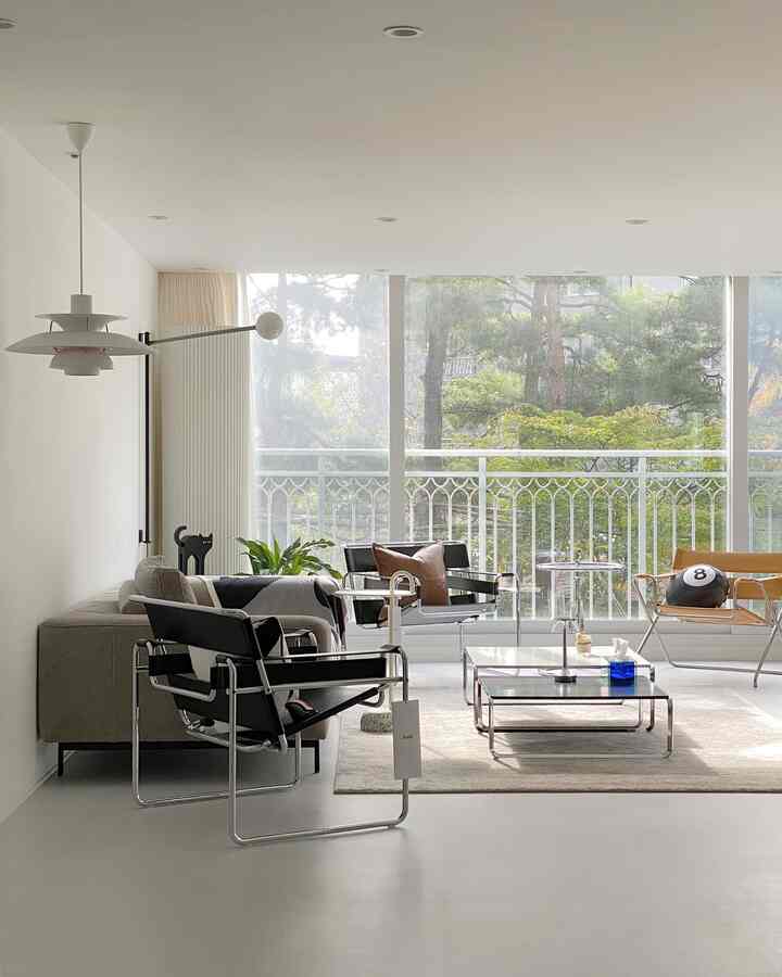 Natural color and white toned living room featuring Mid-Century Modern armchairs, sofa, and a large window with garden view