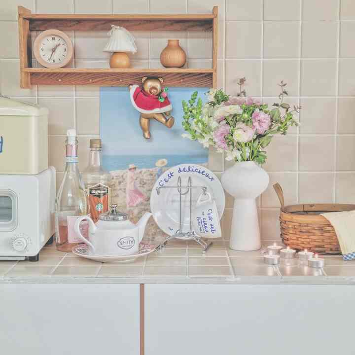 White tiled kitchen space featuring wood tone shelf, vase with flowers, and lit candles creating a cozy atmosphere