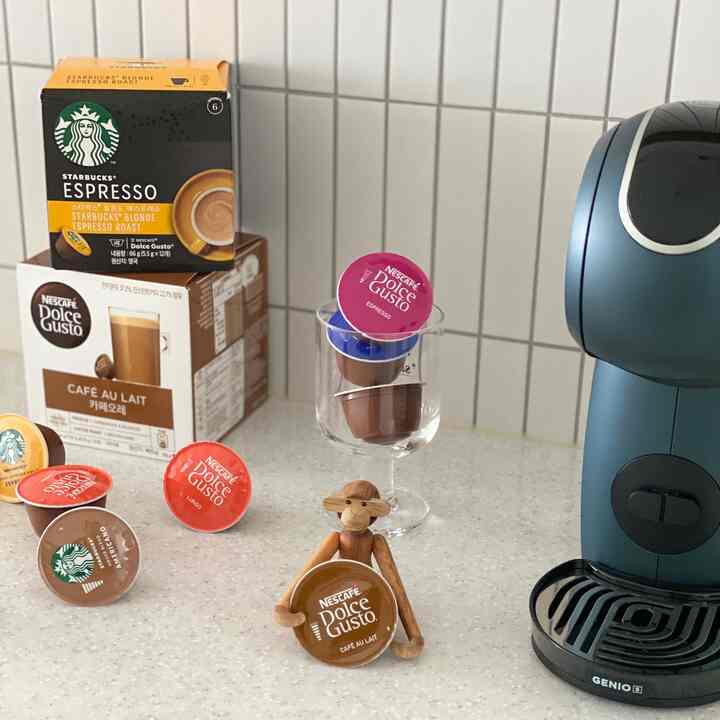白いタイルの壁と明るいカウンターのあるキッチン、カプセルコーヒーマシン、多様なコーヒーカプセル、木製の猿のオブジェが配置されたカフェ風のおうちカフェの空間