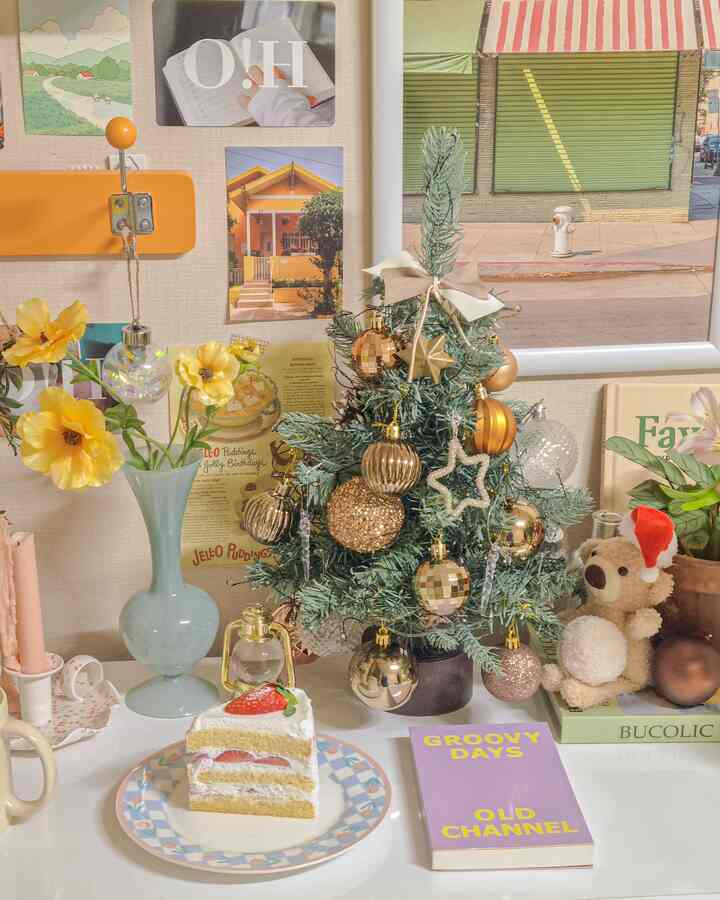 White-toned table featuring yellow flowers, a mini Christmas tree, and a strawberry cake in a cozy setting
