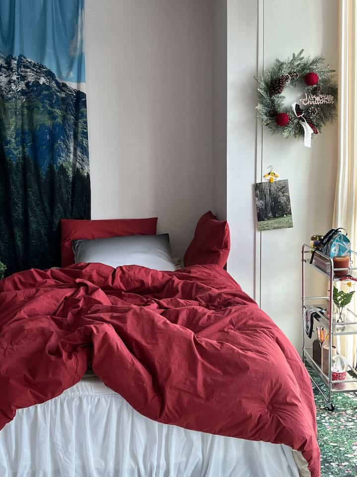 赤と緑の色調が調和するワンルームの寝室、クリスマスリースと整理された収納トロリーが配置された雰囲気のある空間