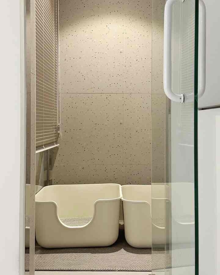 Modern interior featuring two beige litter boxes set on beige tiled floor and wall with blinds on the left side