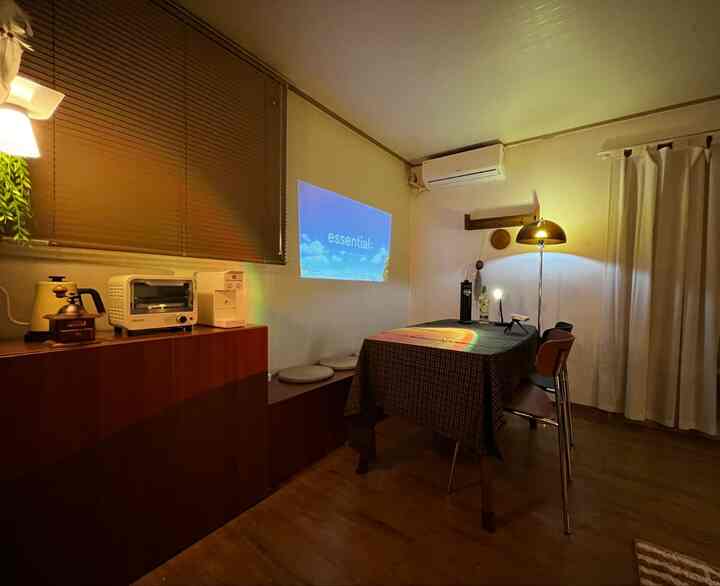 木目調のワンルームダイニングルーム、収納ベンチとダイニングテーブル、プロジェクターが調和する温かみのあるおうちカフェの雰囲気