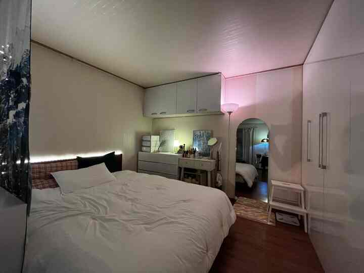 白と木目調の寝室、クイーンサイズベッドと収納家具、全身鏡が配置された落ち着いた雰囲気のあるインテリア