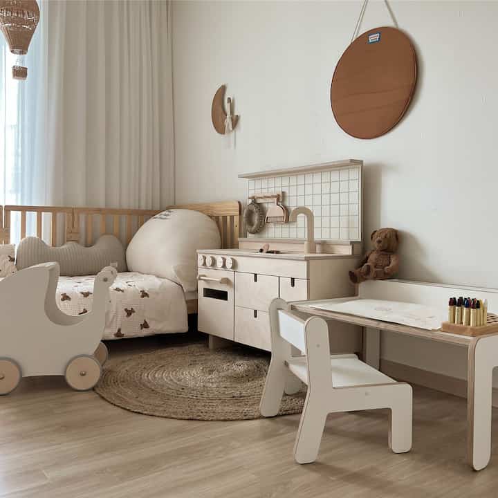 ナチュラルな木目調と白を基調とした子供部屋、ベビーベッドと子供用机、おもちゃのキッチンが配置された落ち着いた空間