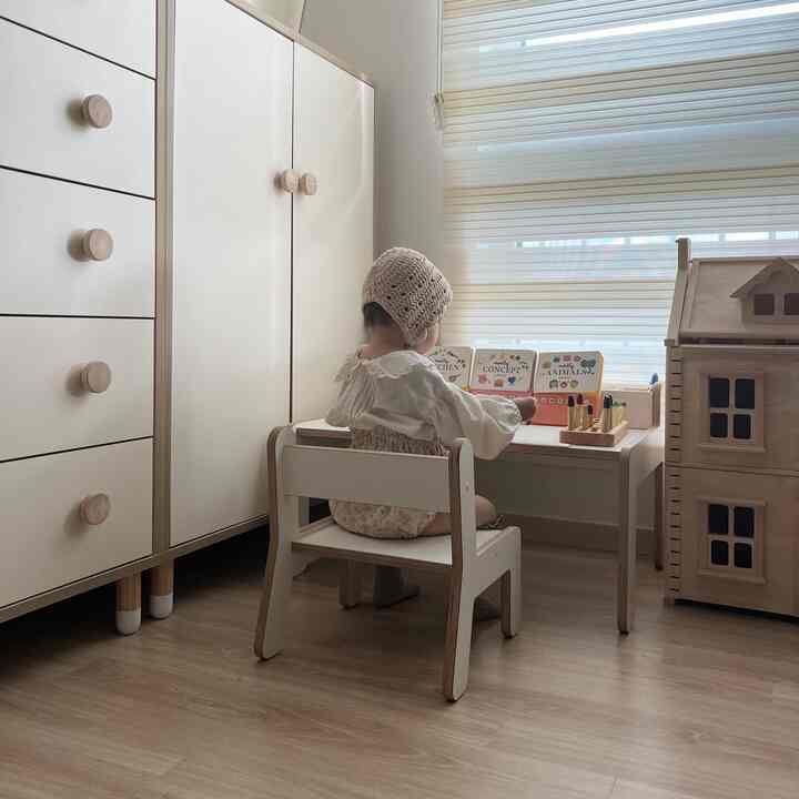 Natural-toned kids' room featuring white desk and chair, toy dollhouse with a cozy atmosphere