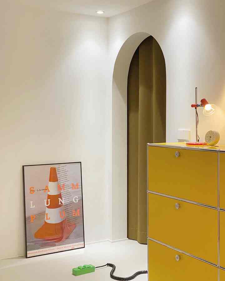 アイボリーの壁と床を背景に、黄色のキャビネットが置かれた、ウォークインクローゼットとパウダールームをつなぐアーチ型の入り口が特徴的な空間